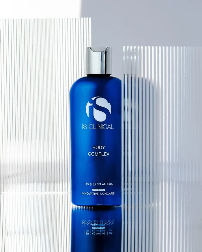 Blue bottle of iS Clinical Body Complex with silver cap against textured white and grey background