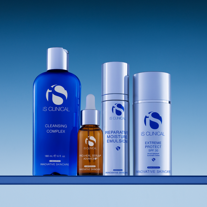 Four iS Clinical skincare products including Cleansing Complex, Pro-Heal Serum Advance+, Reparative Moisture Emulsion, and Extreme Protect SPF 30 on a reflective surface
