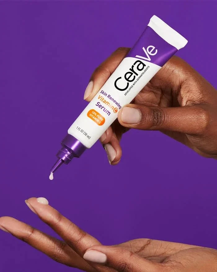 Hand dispensing CeraVe Skin Renewing Vitamin C Serum 30ml tube onto palm, purple background, white tube with purple cap.