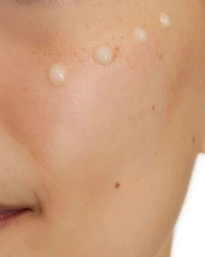 Close-up of CeraVe Skin Renew Vitamin C Serum droplets applied to cheek skin on white background