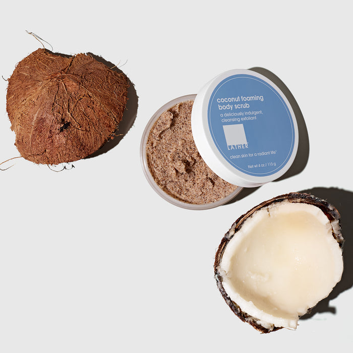 Open jar of Coconut Foaming Body Scrub next to a pieces of a cracked open raw coconut