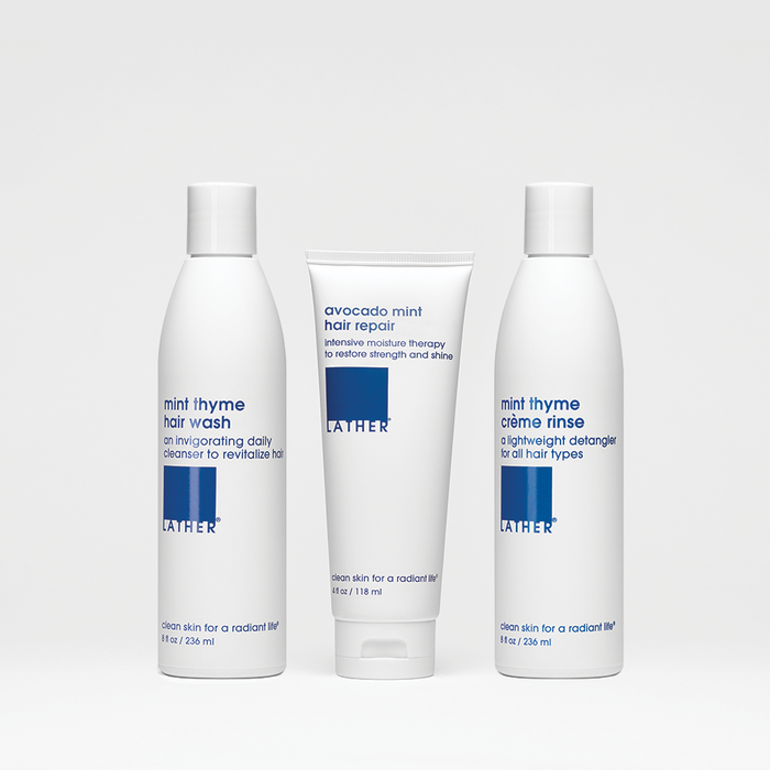 Three bottles of hair care products, including a mint thyme hair wash, mint thyme crème rinse, and avocado mint hair repair, arranged side by side against a white background.