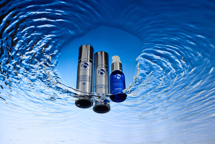 Three iS Clinical skincare bottles submerged in water with ripples and blue background