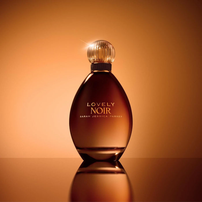 Sarah Jessica Parker Lovely Noir EDP in dark amber bottle with ribbed round cap on warm orange background