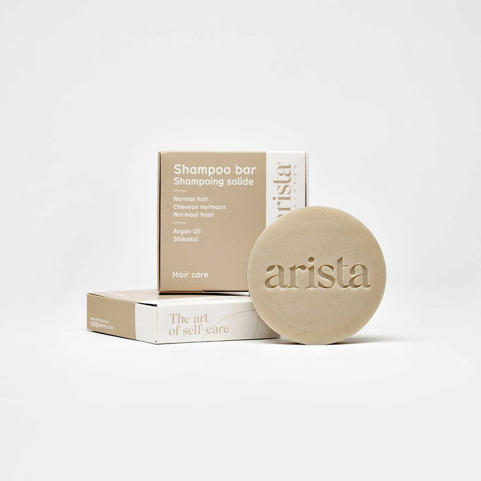 Beige shampoo bar packaging with arista branding and the round bar beside it.
