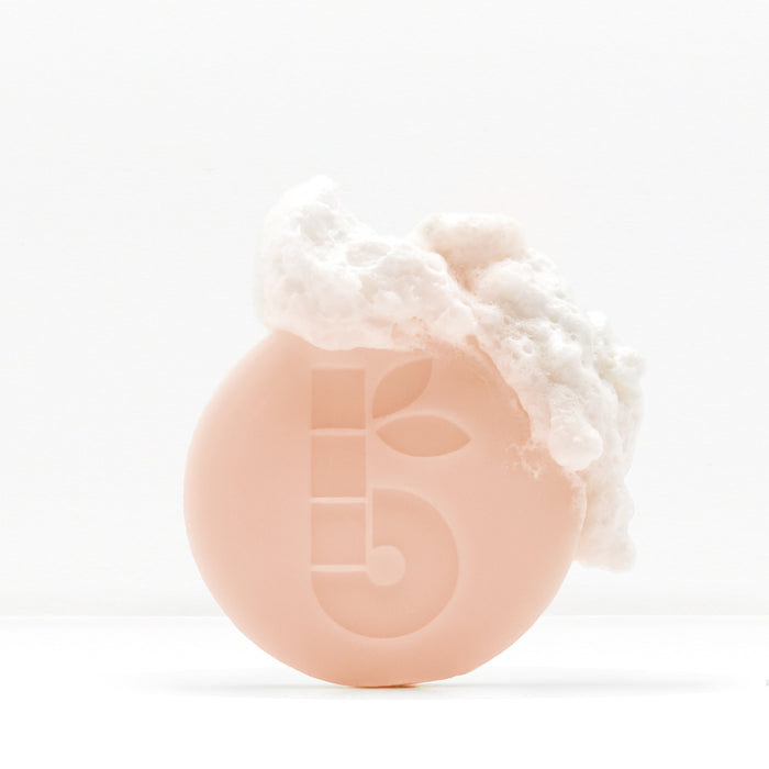 Shaving bar with foamy lather on top held in a hand against a white background