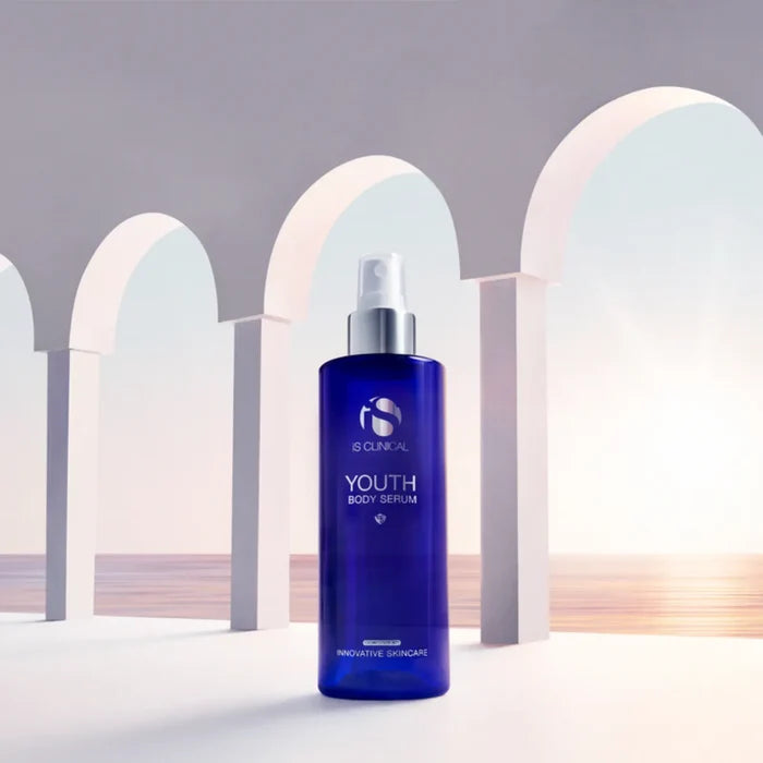 Blue pump bottle of iS Clinical Youth Body Serum with white arches and ocean background