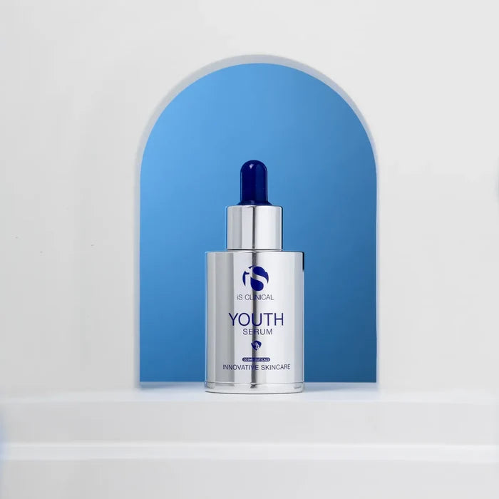 Silver bottle of iS Clinical Youth Serum with blue dropper cap against blue arched background